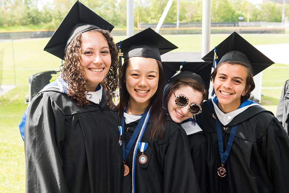 Four students in caps and gowns outdoors after Brandeis Commencement