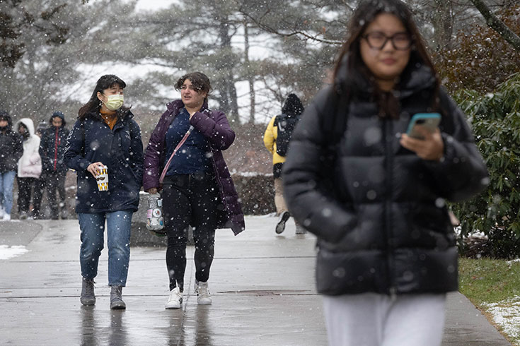 Students walk on campus with snow falling.