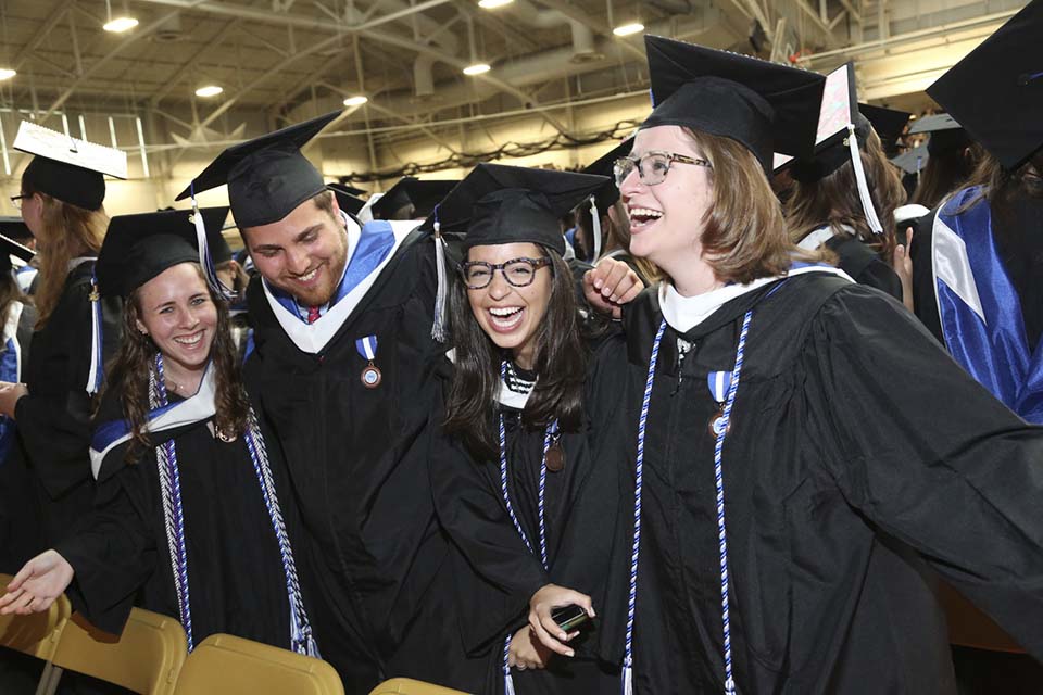 Four graduates (3 women and one man) in cap and gown with big smiles
