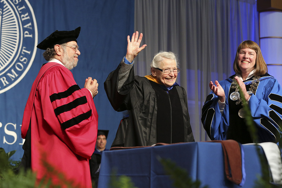 An honorary degree is conferred upon Mildred Dresselhaus, the "queen of carbon science." She waves while Lisa Lynch standing to her left, applauds.