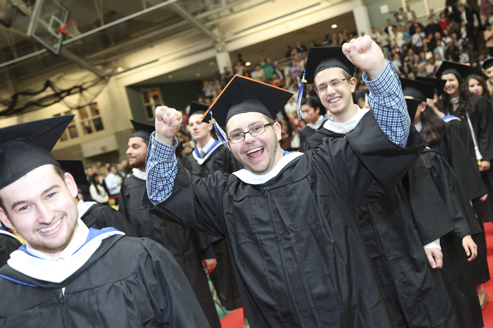 Graduate with both fists raised and huge smile flanked by other very happy, smiling graduates 