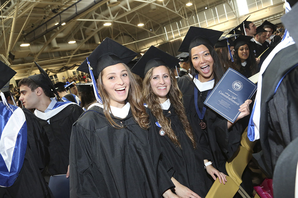 Three friends, enjoying graduation together. One holds up the Commencement program.