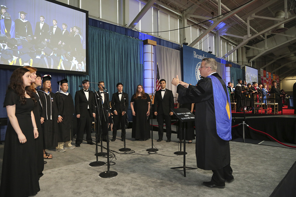 A live performance of the The Brandeis Alma Mater. Student performers stand in a semi-circle as they sing.