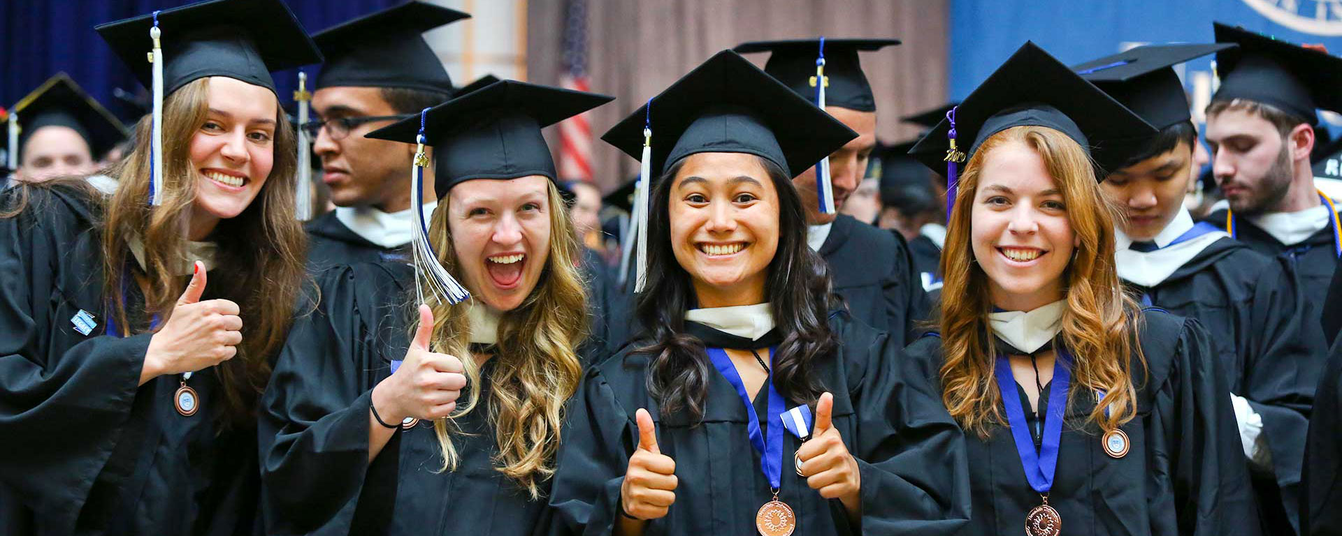 2019 Graduates in caps and gowns smile and give a thumbs up