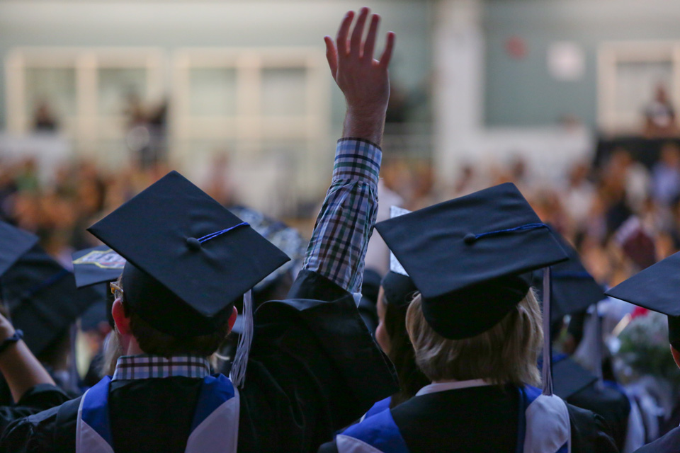 A raised hand in the middle of students in caps and gowns