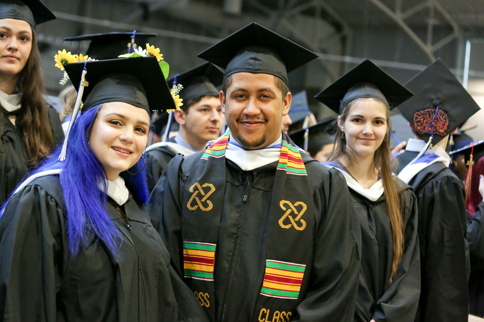 Students, one with blue hair, in caps and gowns