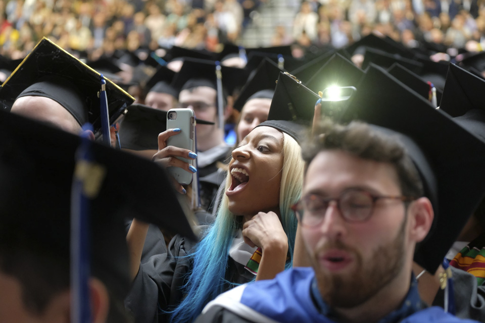 A student surrounded by other students takes a photo with a cell phone