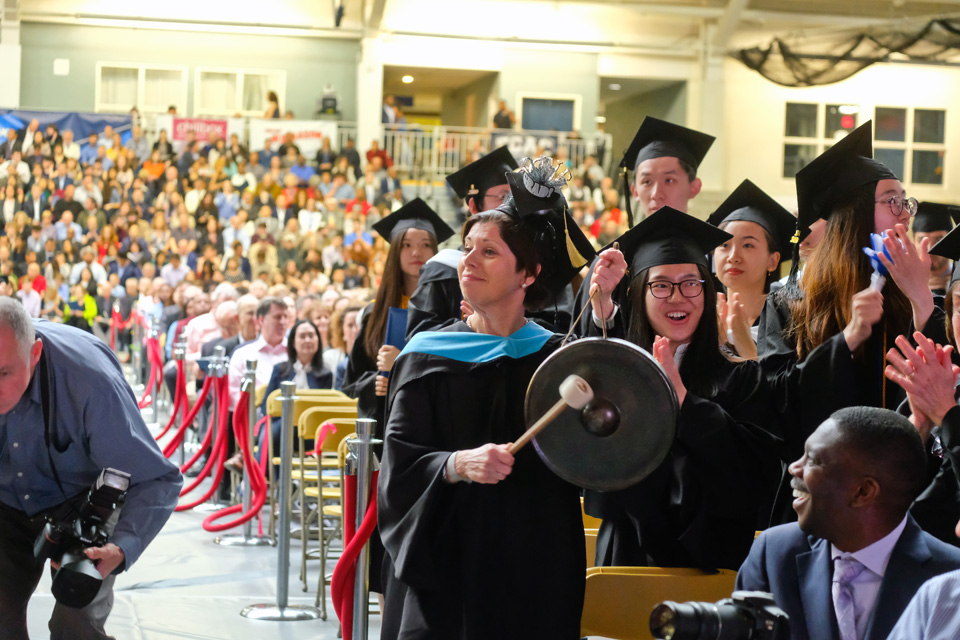 A person in a cap and gown hitting a gong