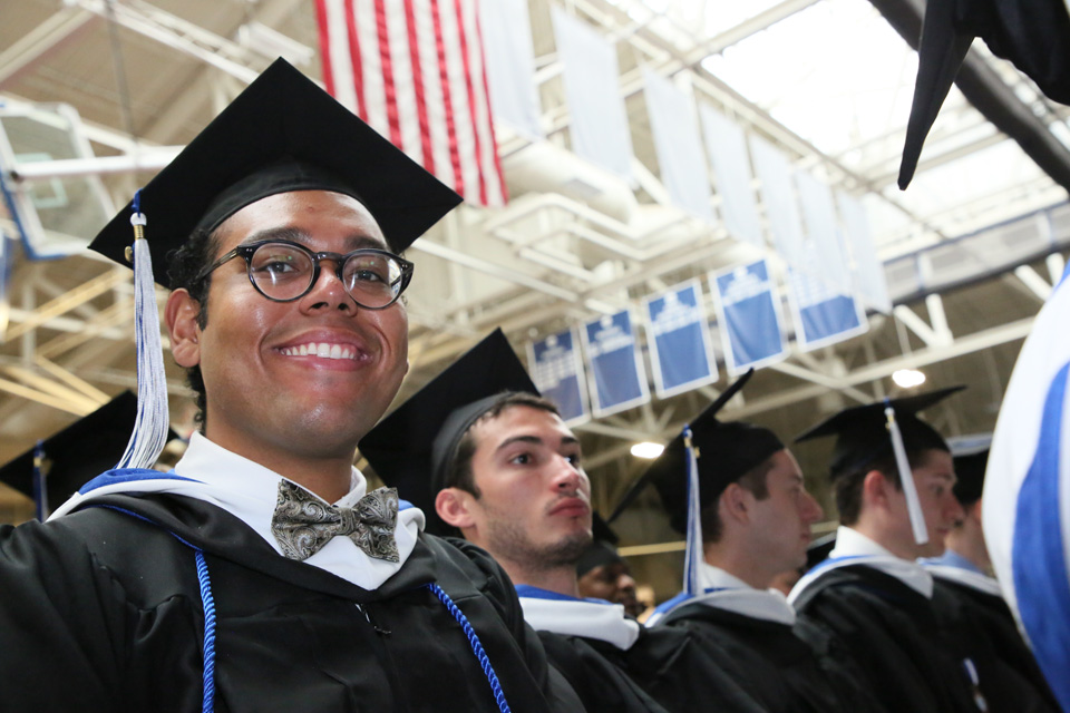 A student in a cap and gown looks down and smiles at the camera