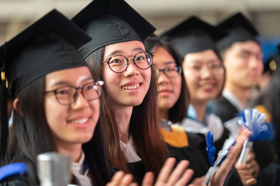 Students clap while looking up at a commencement speaker