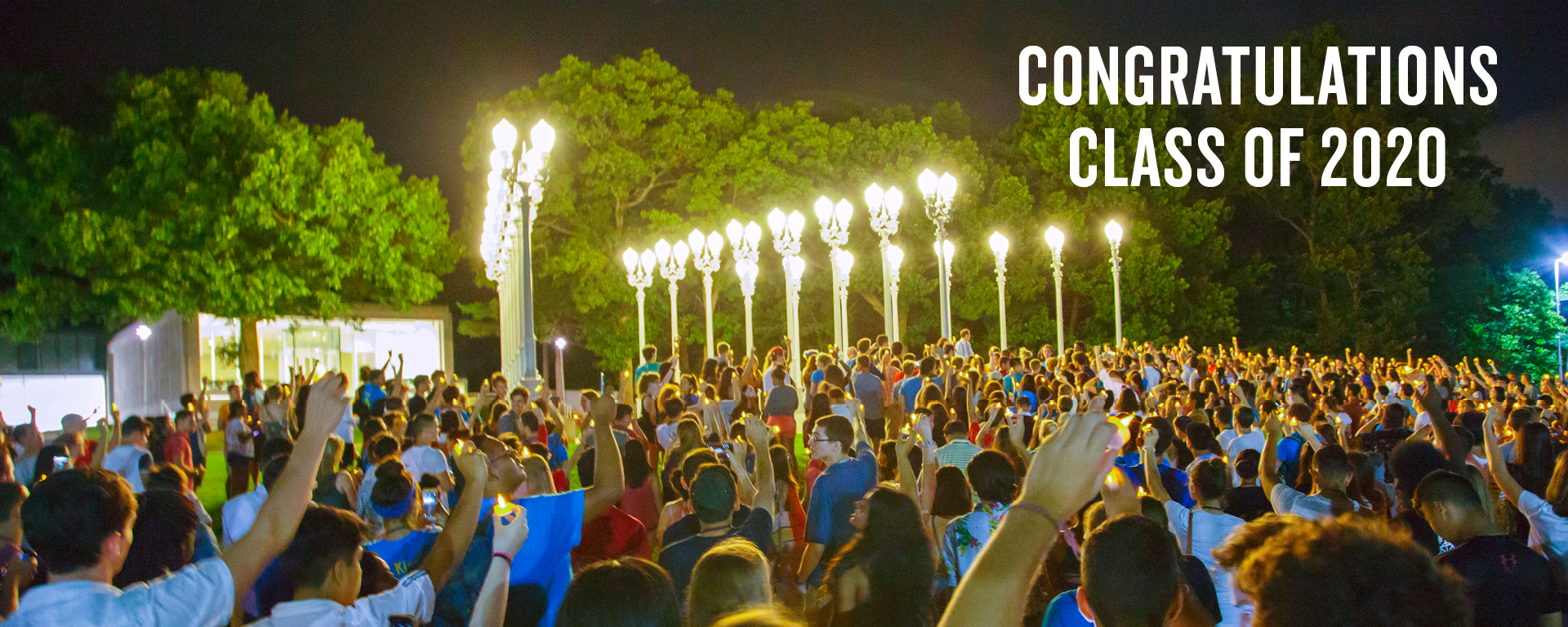 Students stand at night with hands raised, looking at the Light of Reason statue