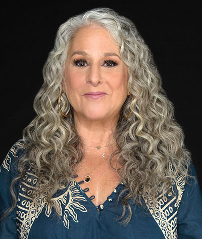 Marta Kauffman smiling at the camera in front of a black background