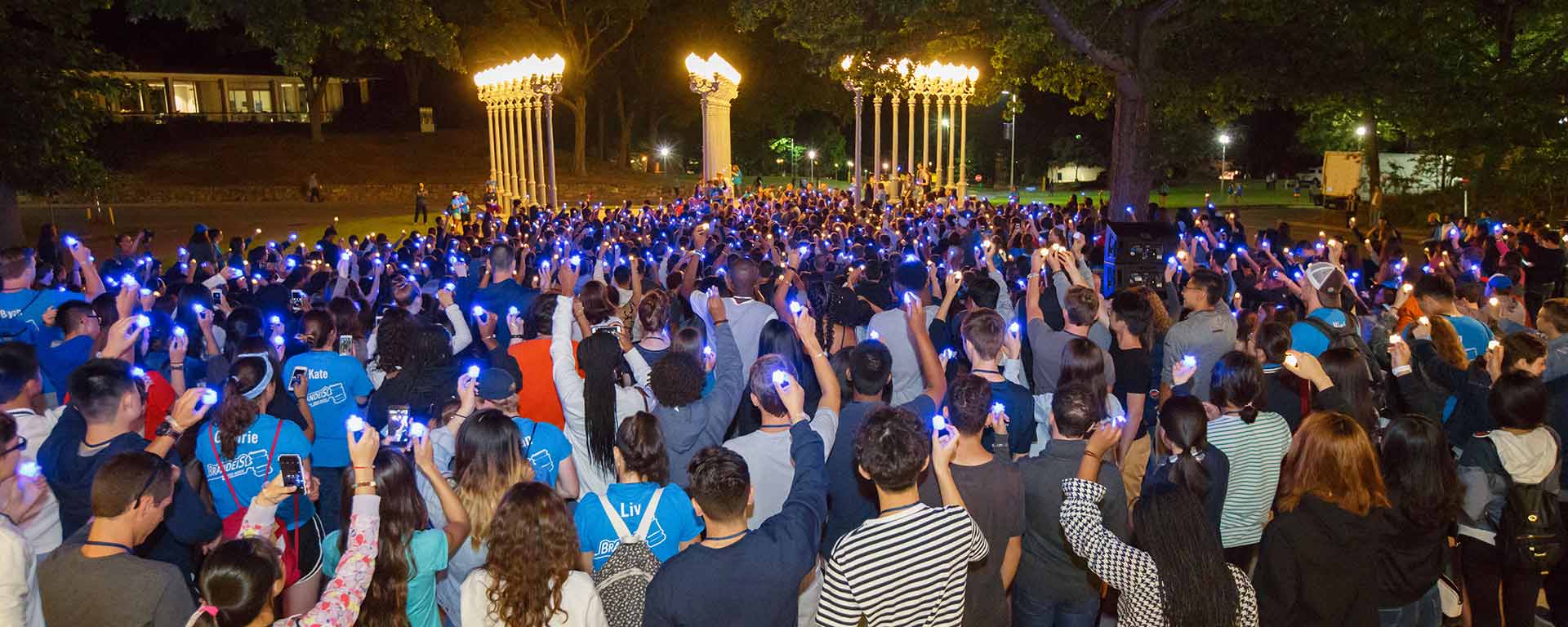 Students stand at night with hands raised, looking at the Light of Reason statue