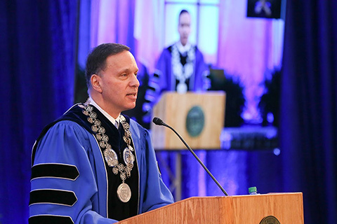 President Ron Liebowitz speaking at a podium in commencement regalia