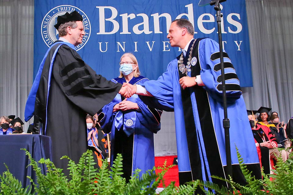 David Harris on the commencement stage shaking hands with President Ron Liebowitz. Provost Carol Fierke stands in the background