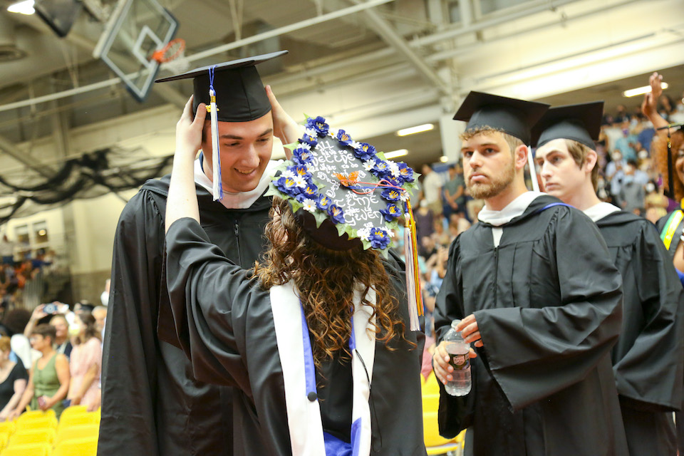 One student fixes another student's cap before the ceremony begins