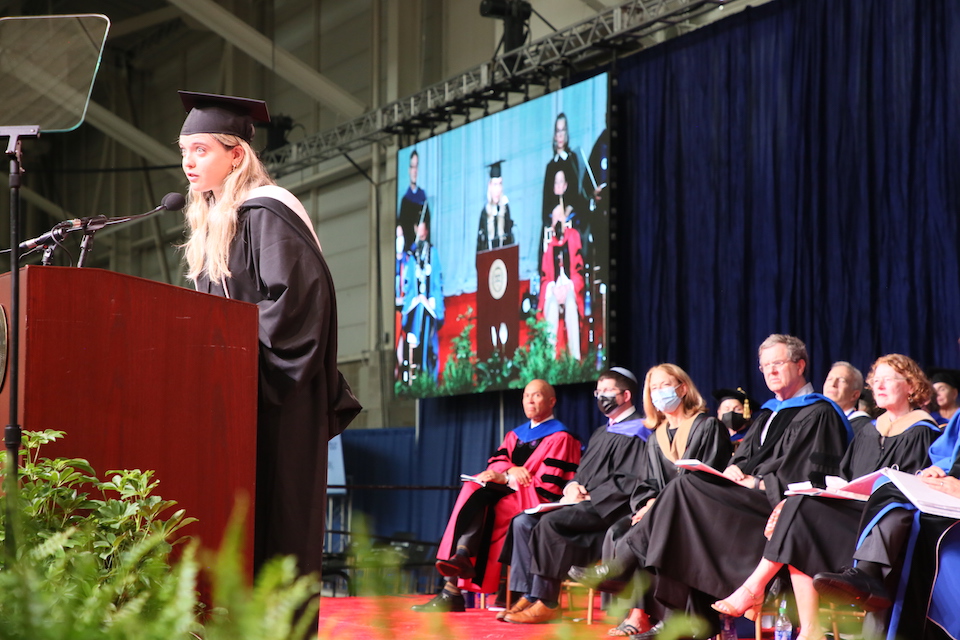 Haley Brown speaks to the audience while other commencement speakers sit behind her.