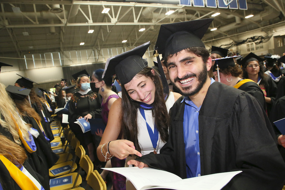 Students smile while looking at the commencement program.