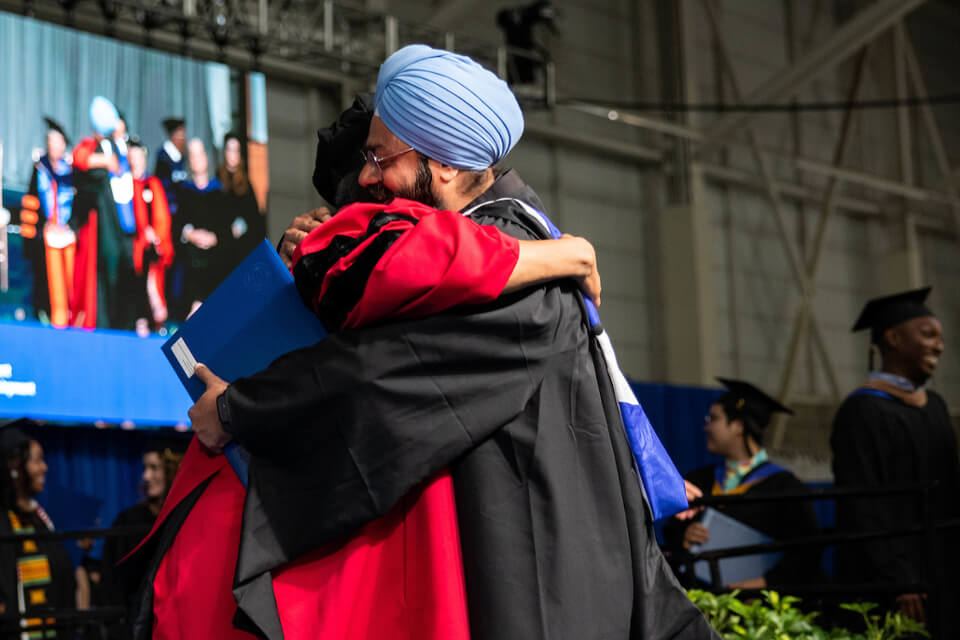 A graduate from the Heller school for Social Policy and Management hugs faculty as they walk the stage.