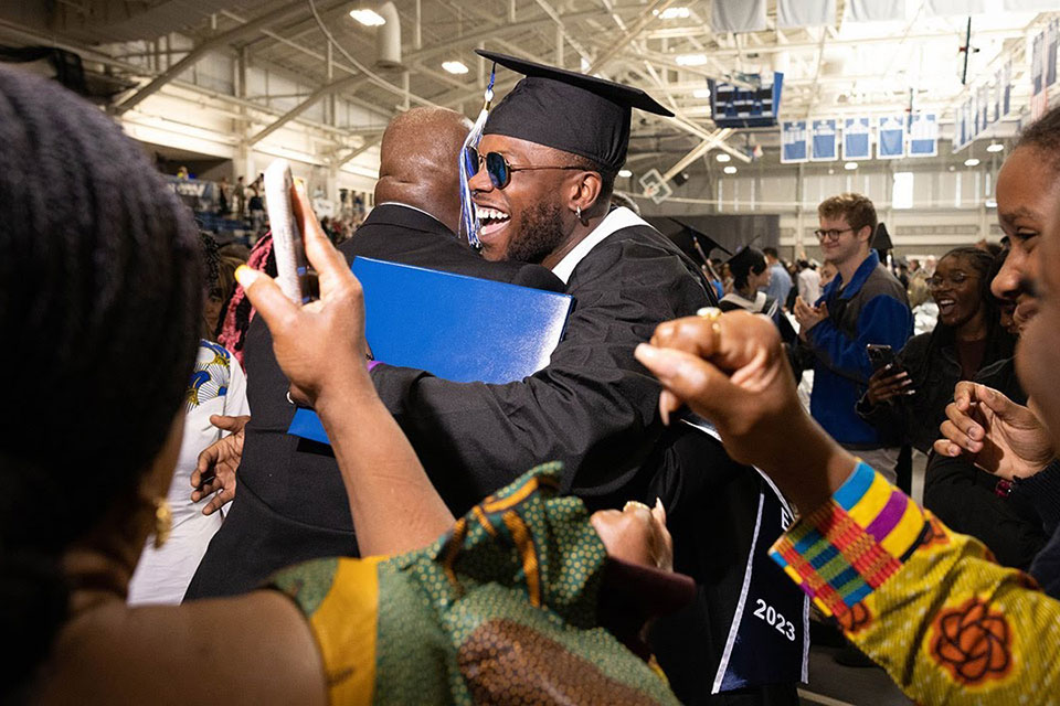 A graduating student hugs a member of the audience while excited family gathers around them