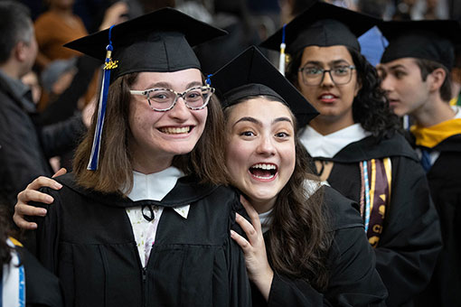 Two graduates smile in their graduation attire.