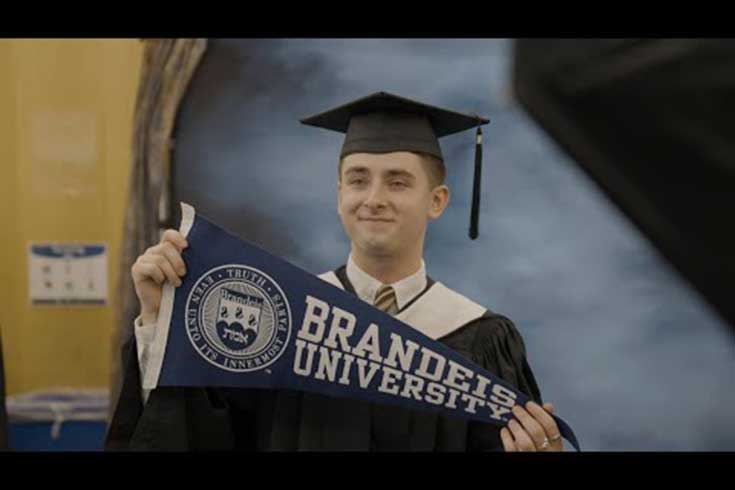 A graduate holding a Brandeis pennant