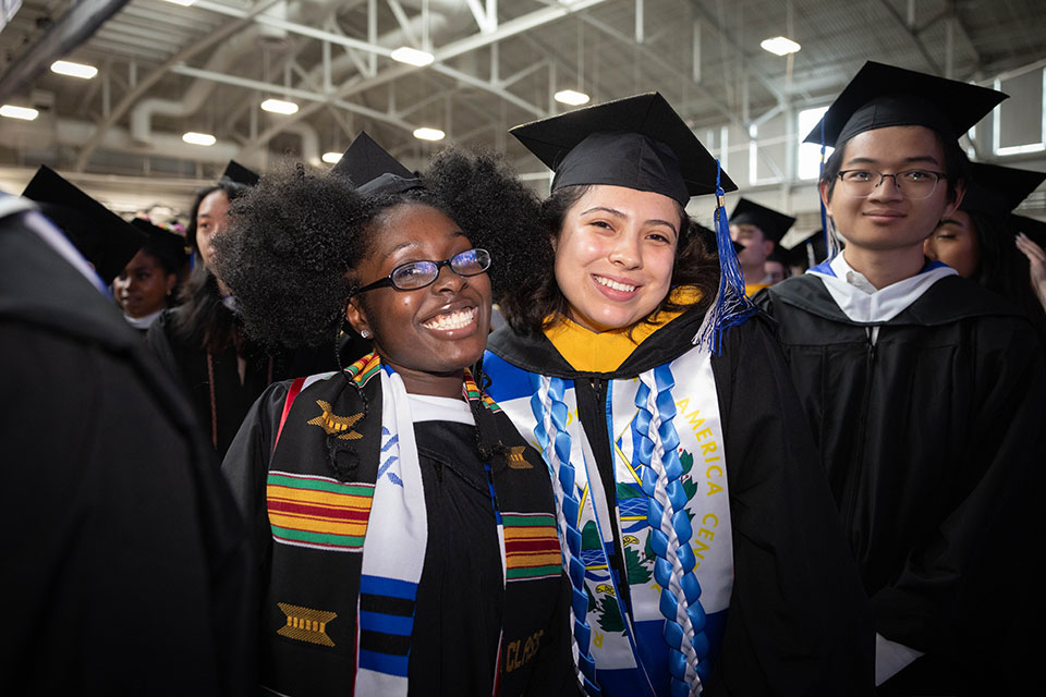Undergraduates in caps and gowns smile in Gosman Sports and Convocation Center