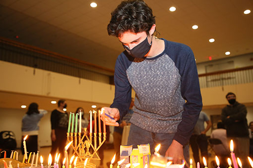 A student in a mask lights a Hanukkah candle