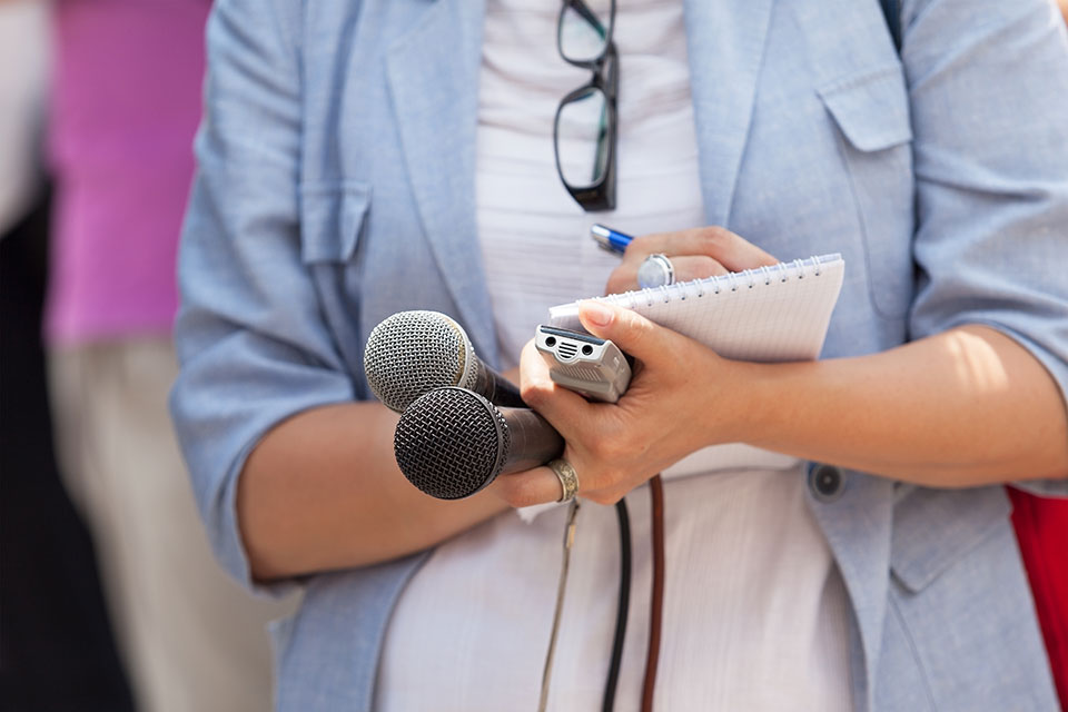 Close up of a reporter taking notes with microphones in their hand