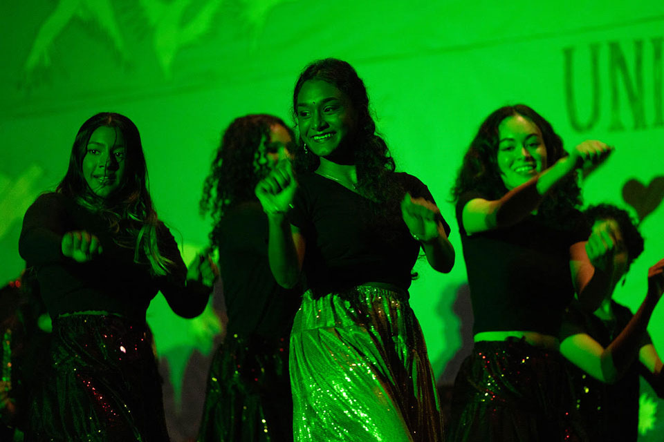 Students dance on stage under a green light.