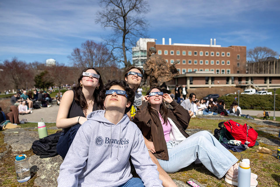 Four students wearing eclipse glasses look up to the sky.
