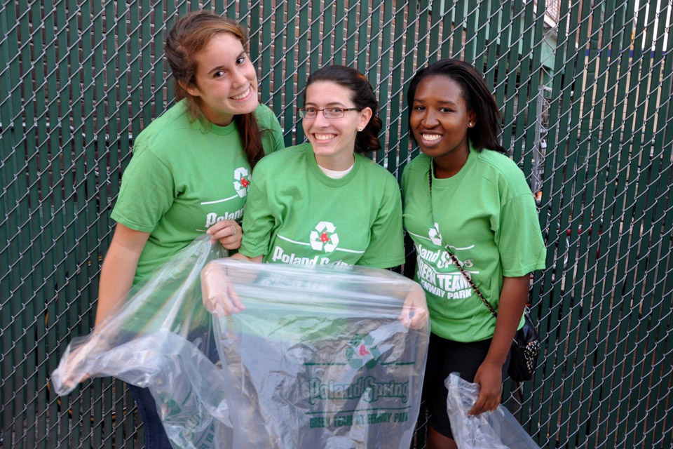 Three students wearing green shirts holding trash bags as part of a cleanup