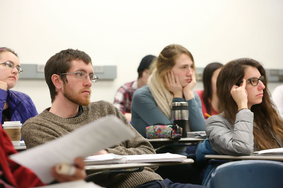 Three students sitting in a classroom look toward the front of the room
