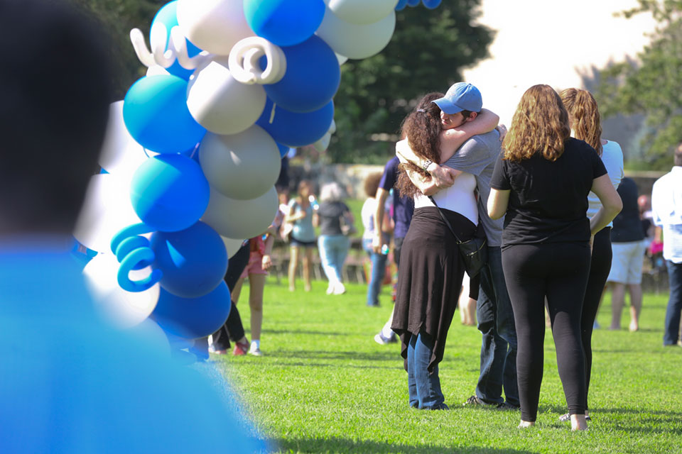 Two family members hug under a blue and white balloon arch