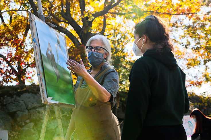 Susan Lichtman stands behind a student who is painting at an easel outside