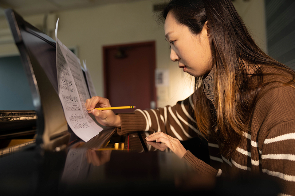 Aris Wang sits at a piano making a note on a music sheet with a pencil