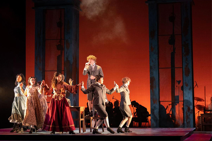 Actors on stage in front of a red background. Actors are dancing and singing.