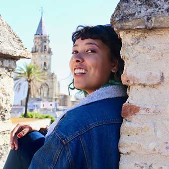 Aviva Davis sitting with her back to a concrete wall outdoors