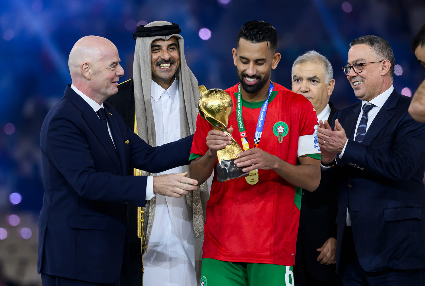 Gianni Infantino stands on a stage with the Emir of Qatar Sheikh Tamim bin Hamad Al-Thani as they hand the FIFA Arab Cup 2025 trophy to Mohamed Hrimat of Morocco.