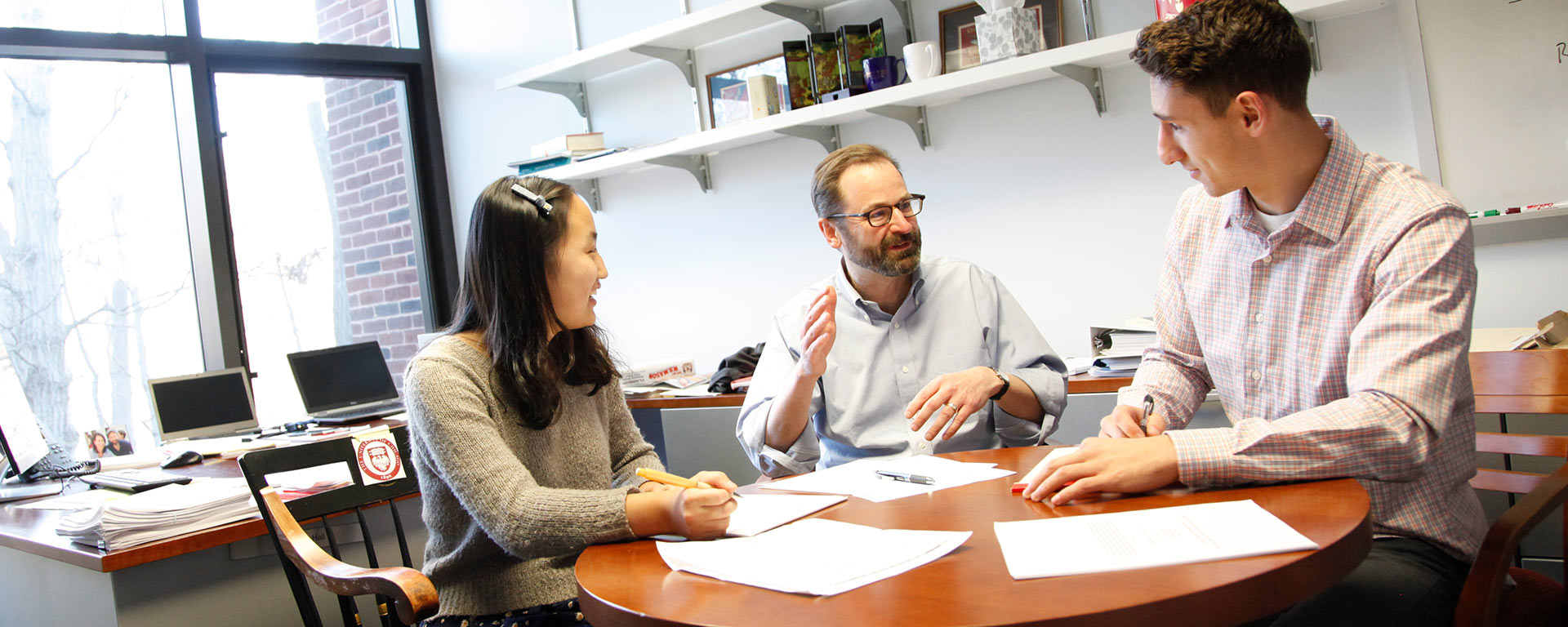 Two students sitting at a table in an office with Professor Hall