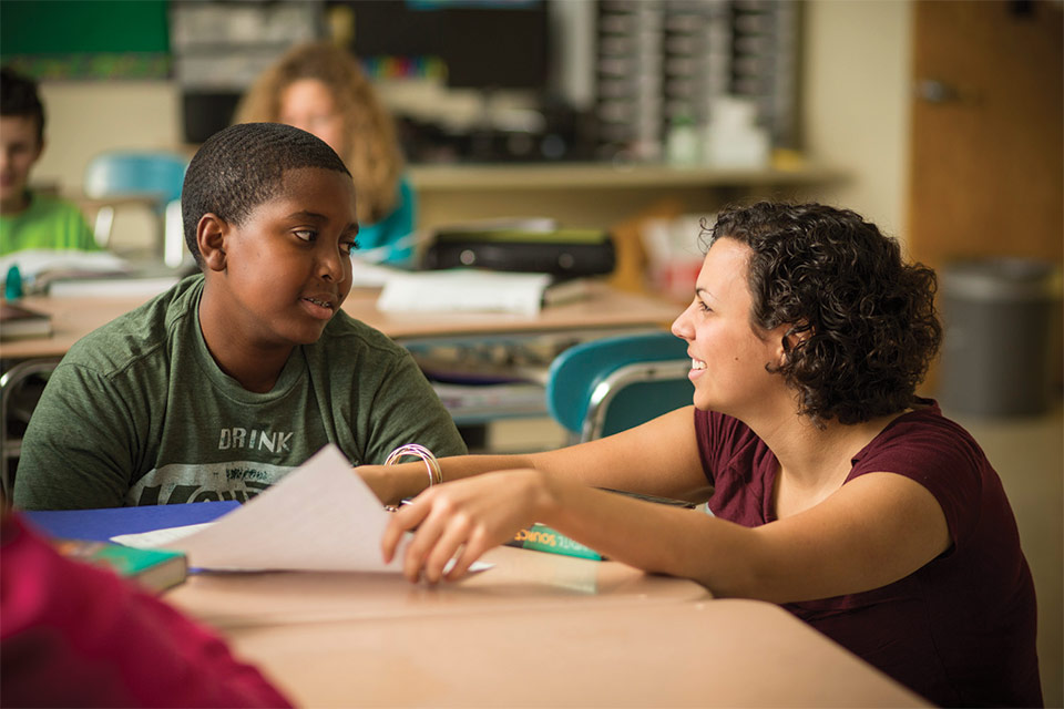 A smiling teacher engages with an elementary student