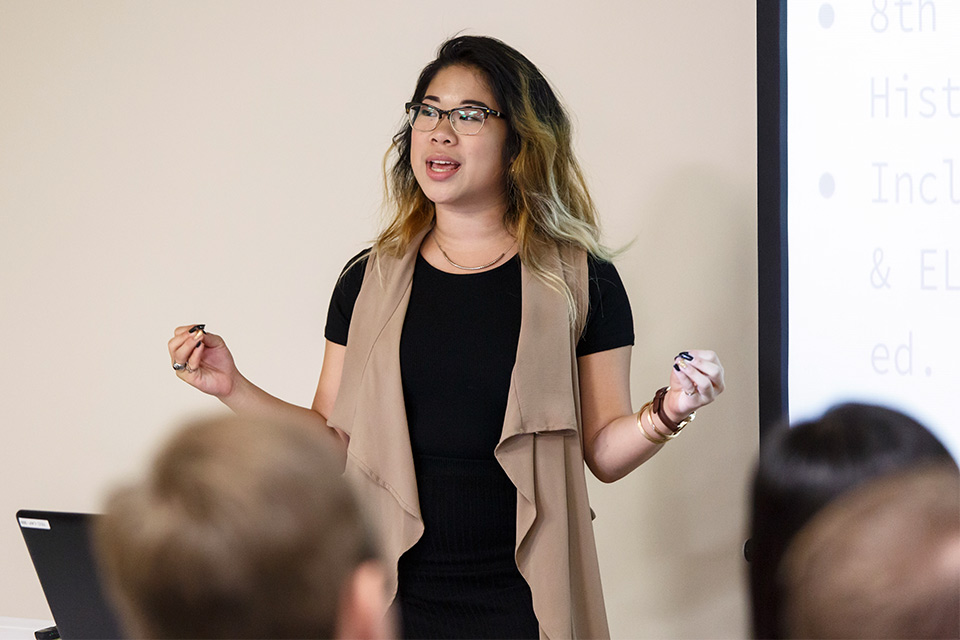 A young teacher stands before a projection screen