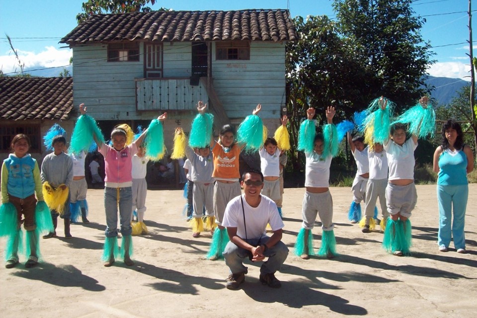 students dancing in costume in front of building and mountains, with Chris Lau on the ground in front of them