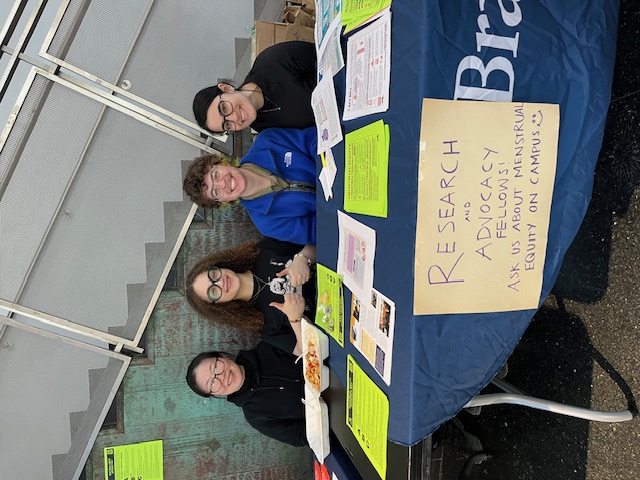 four students sitting at a table with a sign that reads: "research and advocacy fellows: ask us about menstrual equity on campus"