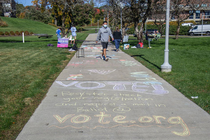 Student walking down sidewalk, which has chalk messages promoting voting.