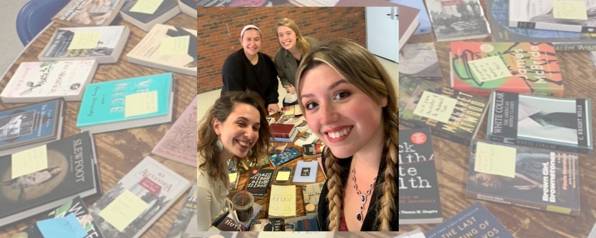 Undergraduate Department Representatives Cayenn Landau, Hannah Heimann, Irina Znamirowski, and Autumn Bellan smile for a selfie in front of a transparent image of the books brought to the Meet the Major / Book Exchange event.