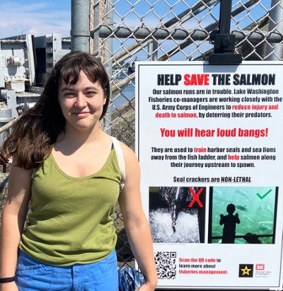 Katy Tanzer stands by a sign next to the Ballard Locks which connects Lake Union and the Puget Sound