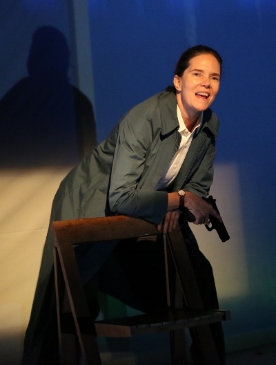 An actor stands on stage with a gun