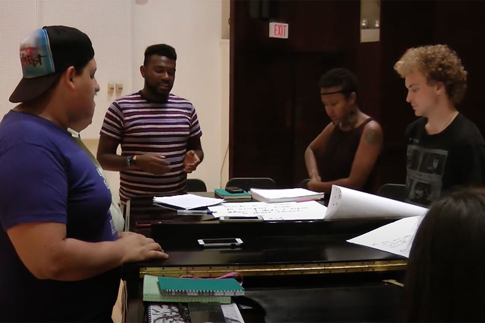 A group of students talks around a piano