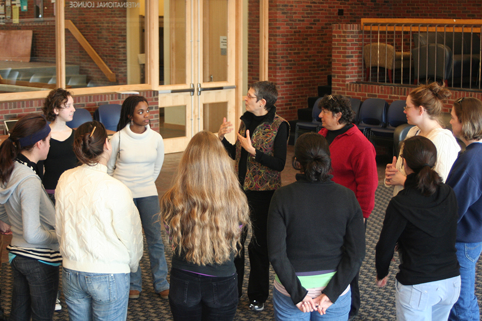 A small group stands in a circle listening to someone talk